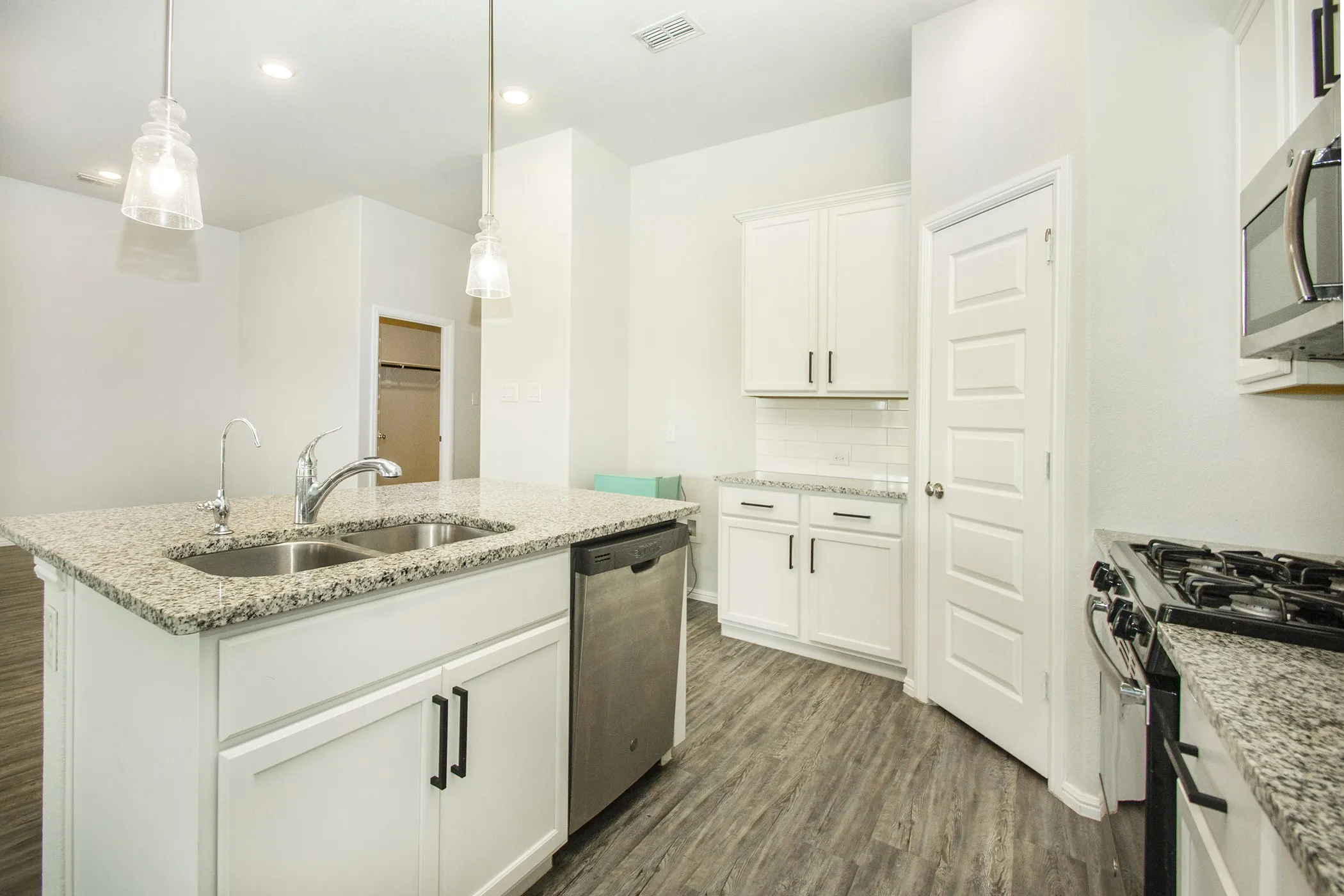Kitchen featuring dark wood-style floors, appliances with stainless steel finishes, white cabinetry, a kitchen island with sink, and hanging light fixtures
