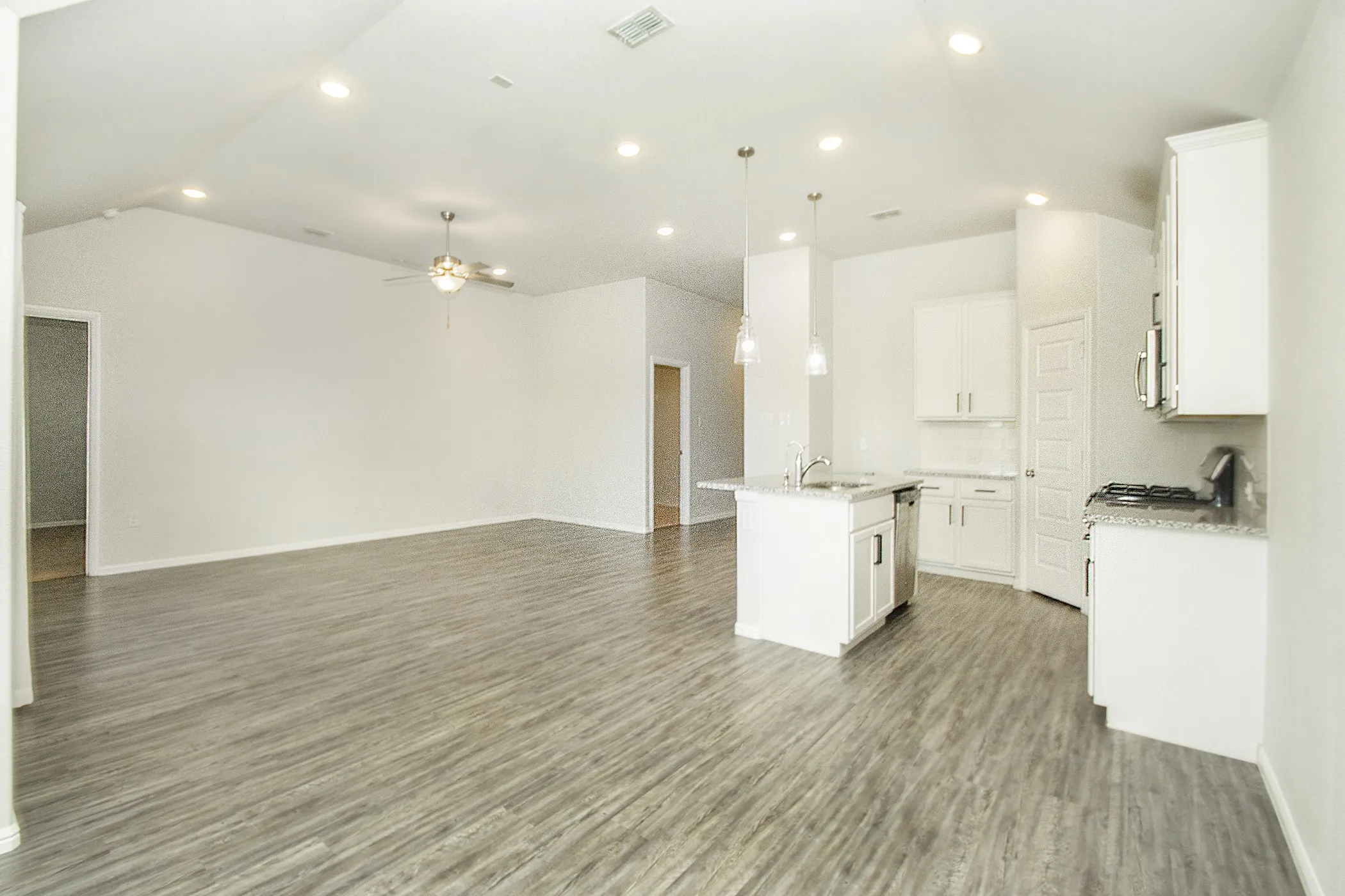 Kitchen featuring open floor plan, a center island with sink, a ceiling fan, wood finished floors, and lofted ceiling