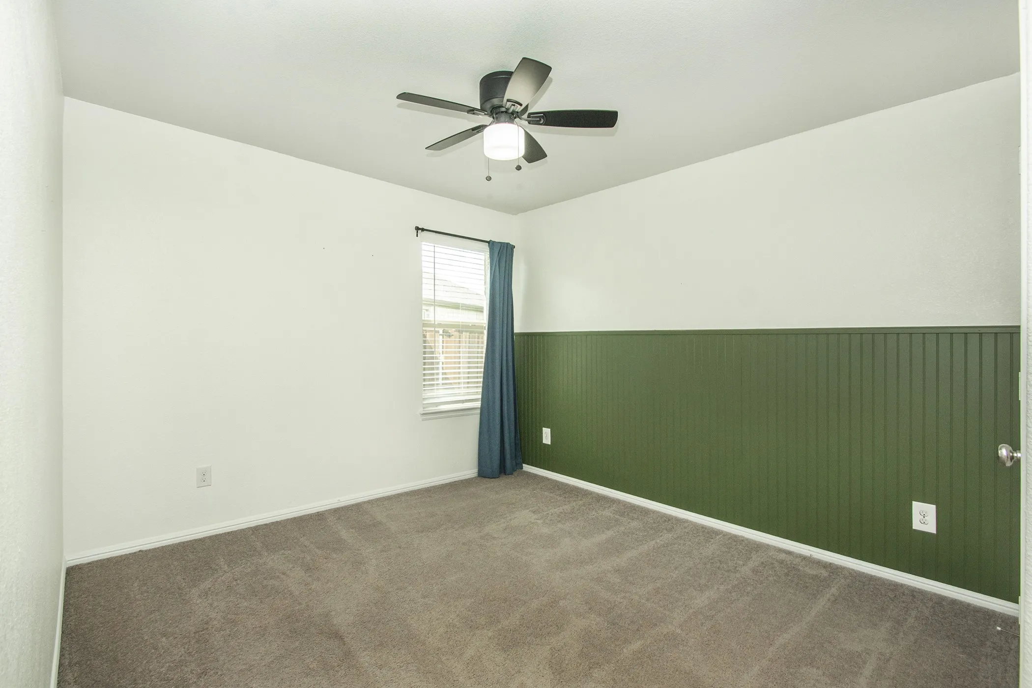 Carpeted empty room featuring ceiling fan and wainscoting