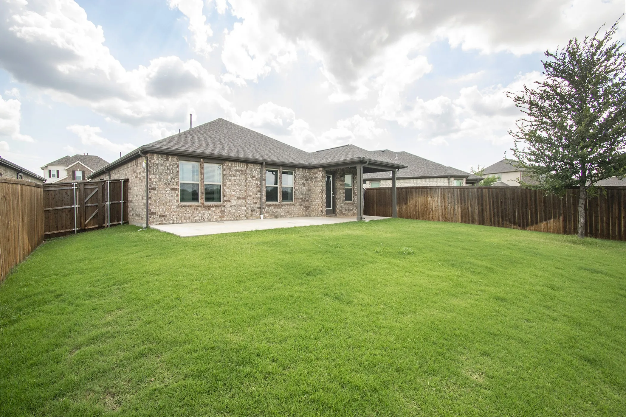 Rear view of property with a shingled roof, brick siding, a patio, and a fenced backyard