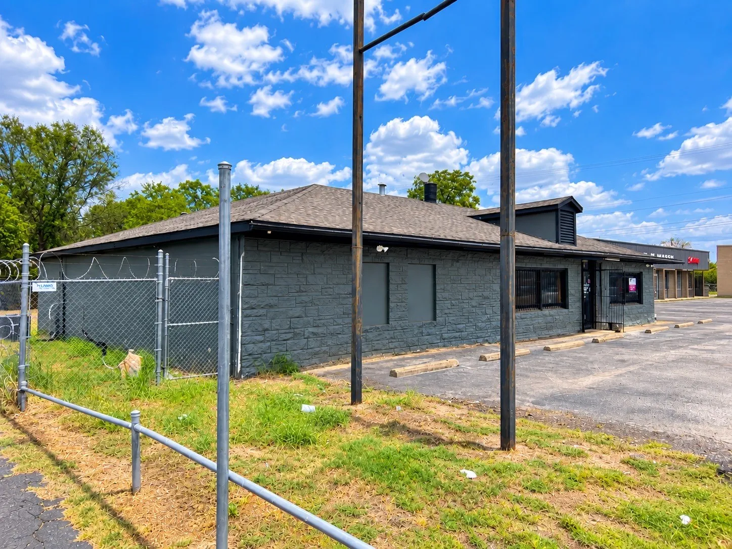 Building exterior featuring dark gray stone-finish siding, a dark asphalt shingle roof, a chain-link fence, and an asphalt parking area