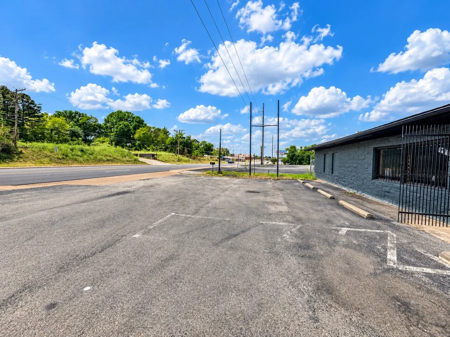 Asphalt parking lot, painted parking space indicators, building exterior with textured finish, prominent window, and metal security gate