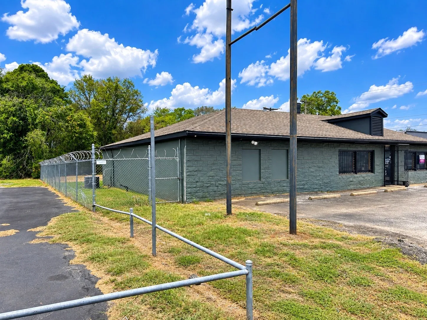 Brick exterior with a shingled roof, featuring a chain-link fence with barbed wire and an asphalt parking area