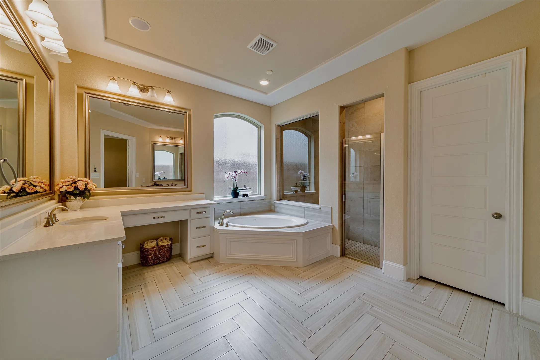 Spacious master bathroom featuring a corner jetted tub, glass-enclosed shower, a double vanity with ample counter space, and a dedicated vanity seating area and designer tile