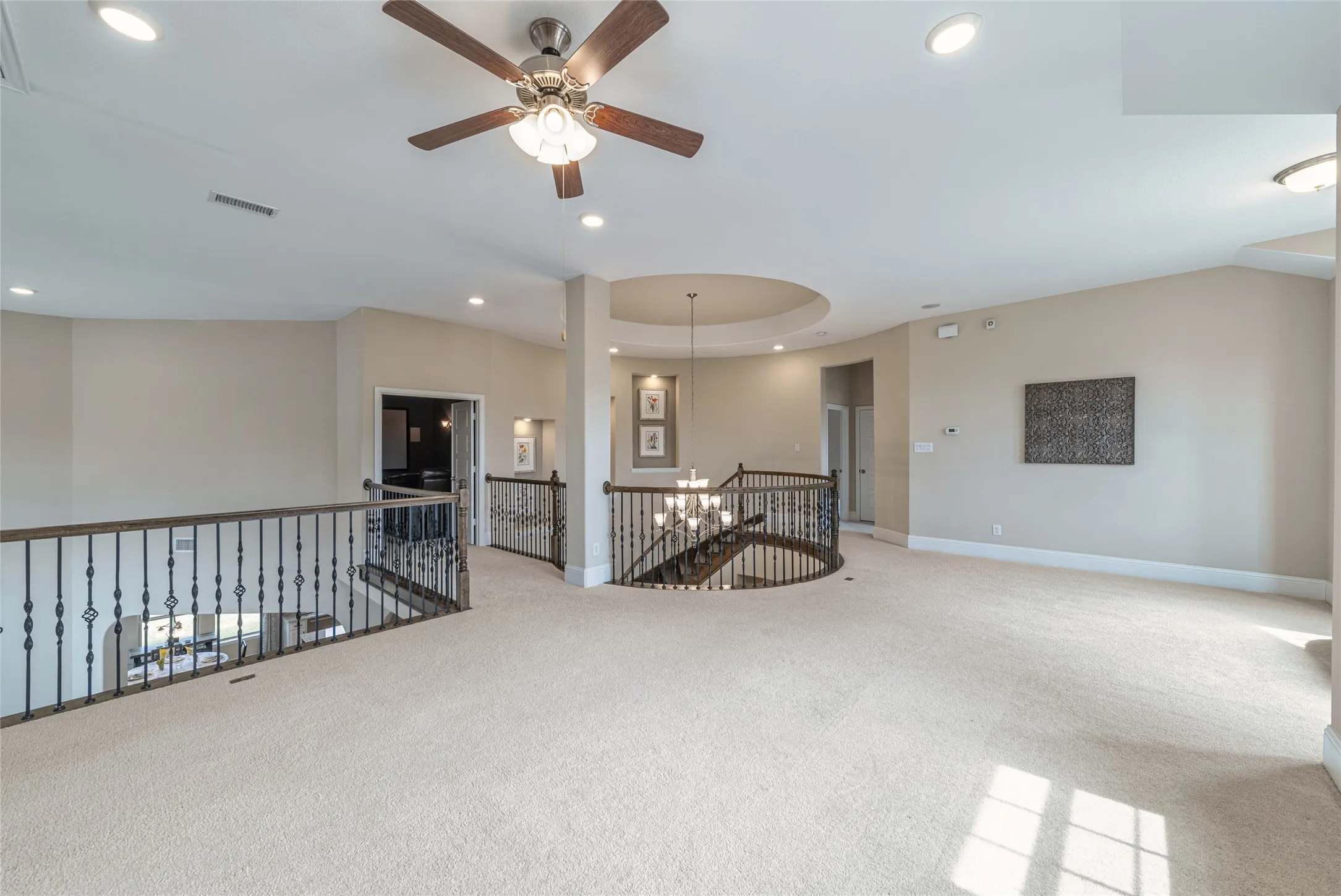 Spacious carpeted upper-level landing featuring a wood-finish ceiling fan, recessed lighting, and ornate wrought iron railings