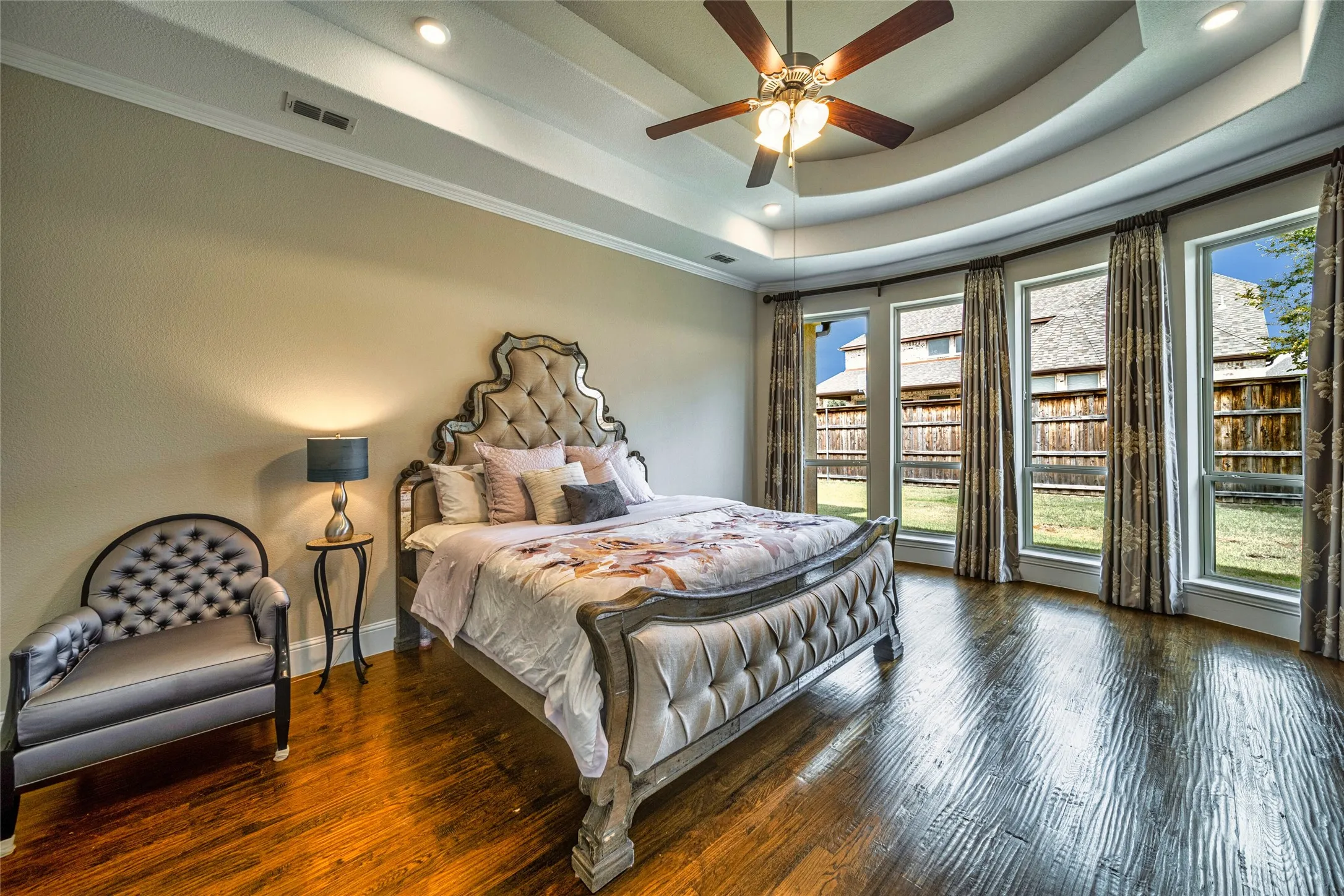 Tray ceiling with recessed lighting, wood-finish flooring, ceiling fan, and a curved wall of multiple windows