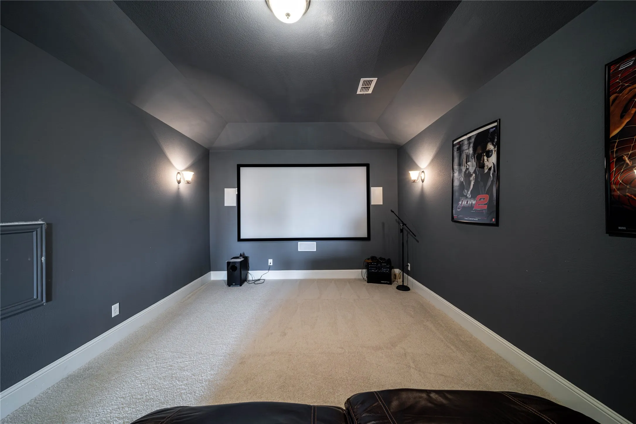 Dedicated media room featuring a projection screen, built-in wall speakers, and wall sconce lighting