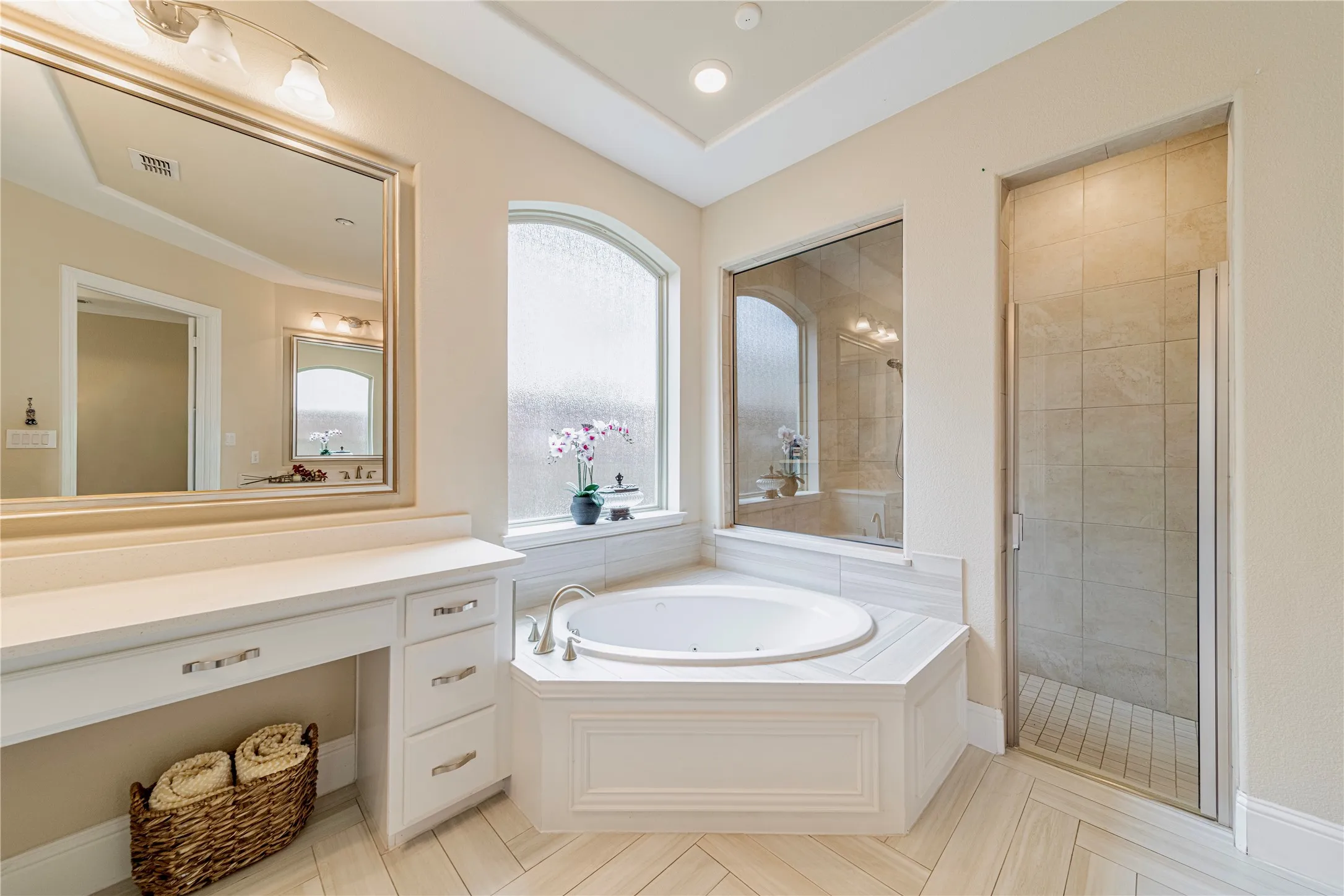 Spacious master bathroom featuring a corner jetted tub, glass-enclosed shower, a double vanity with ample counter space, and a dedicated vanity seating area and designer tile