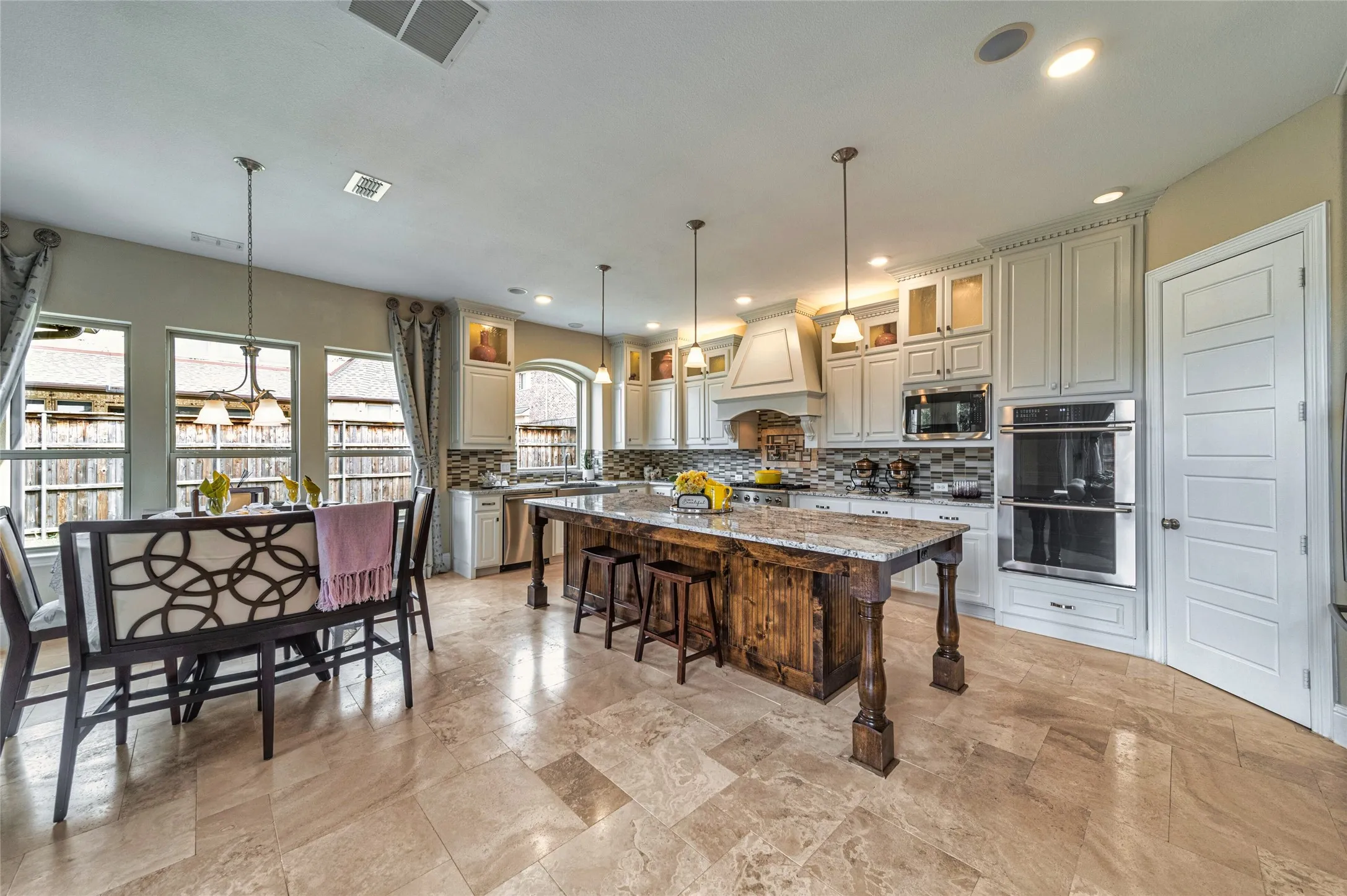 Kitchen featuring a large wood-finish island with stone countertop, white cabinetry with glass upper doors, mosaic tile backsplash, and stainless steel double ovens