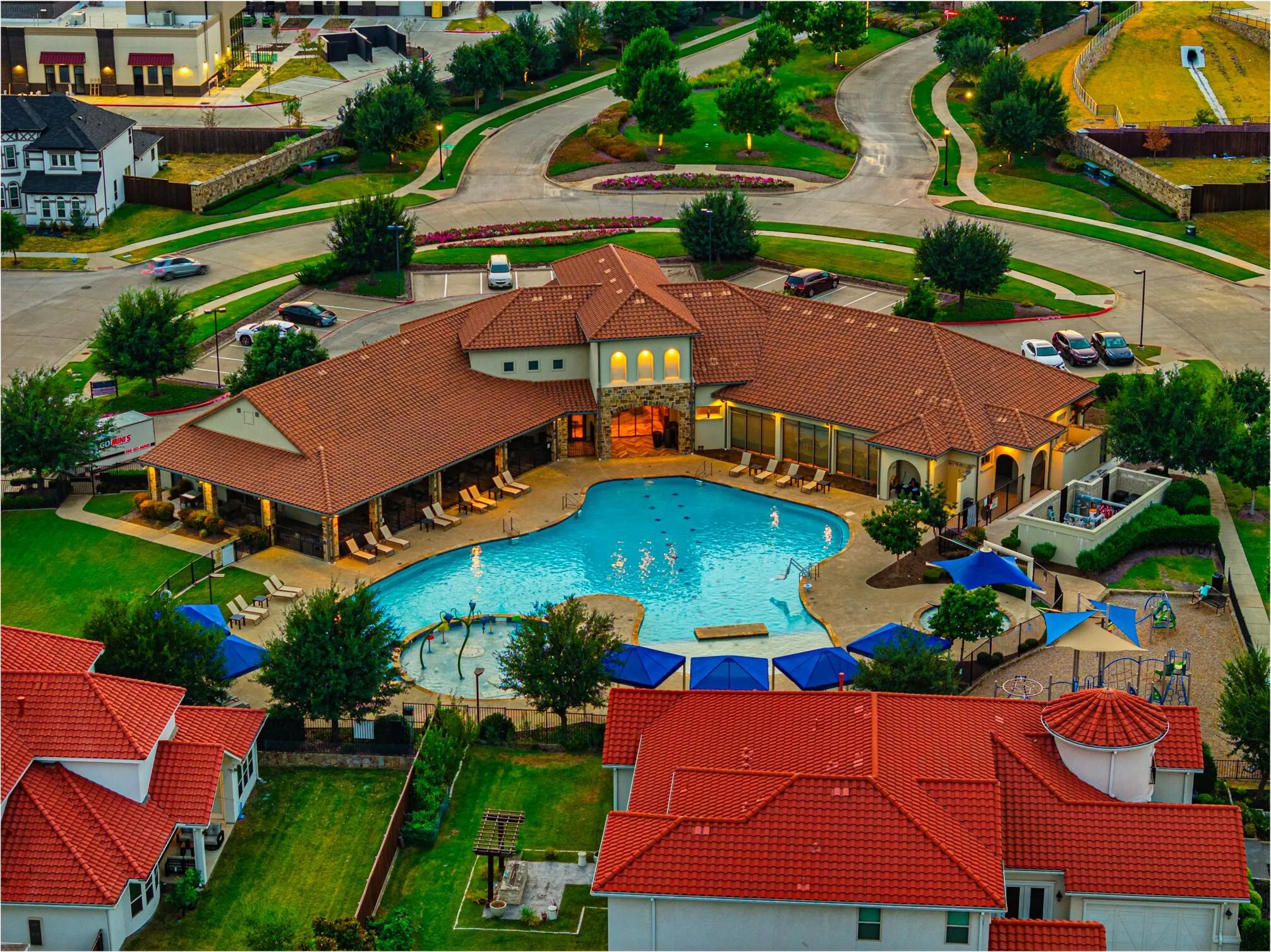 Community pool with multiple entry points, adjacent shaded lounge areas, and a children's splash pad