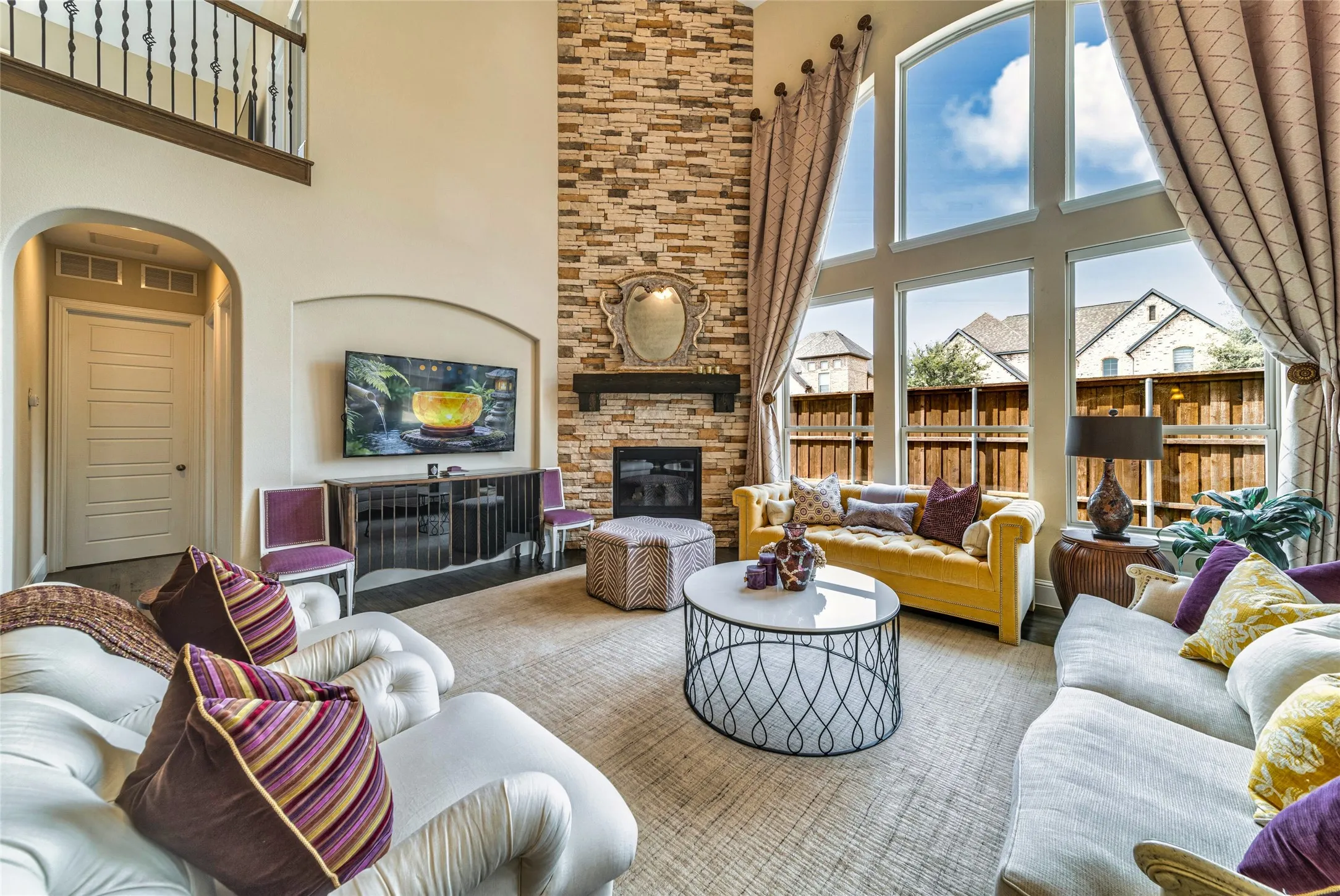 Two-story living area featuring a stacked stone fireplace, large picture windows, and a wrought iron balcony overlooking the space