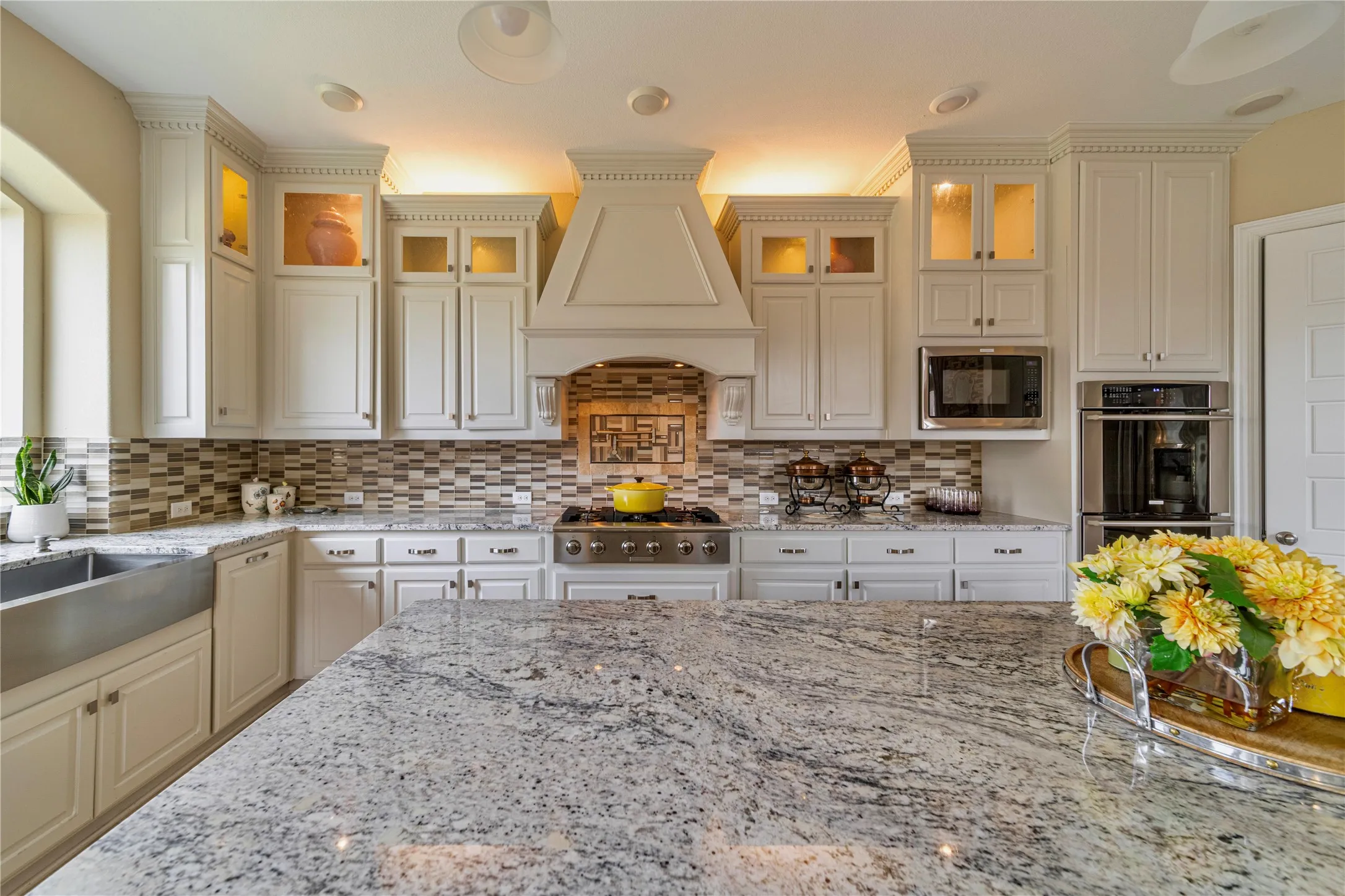 Granite countertops with an integrated island, white cabinetry with crown molding, stainless steel appliances, and a mosaic tile backsplash