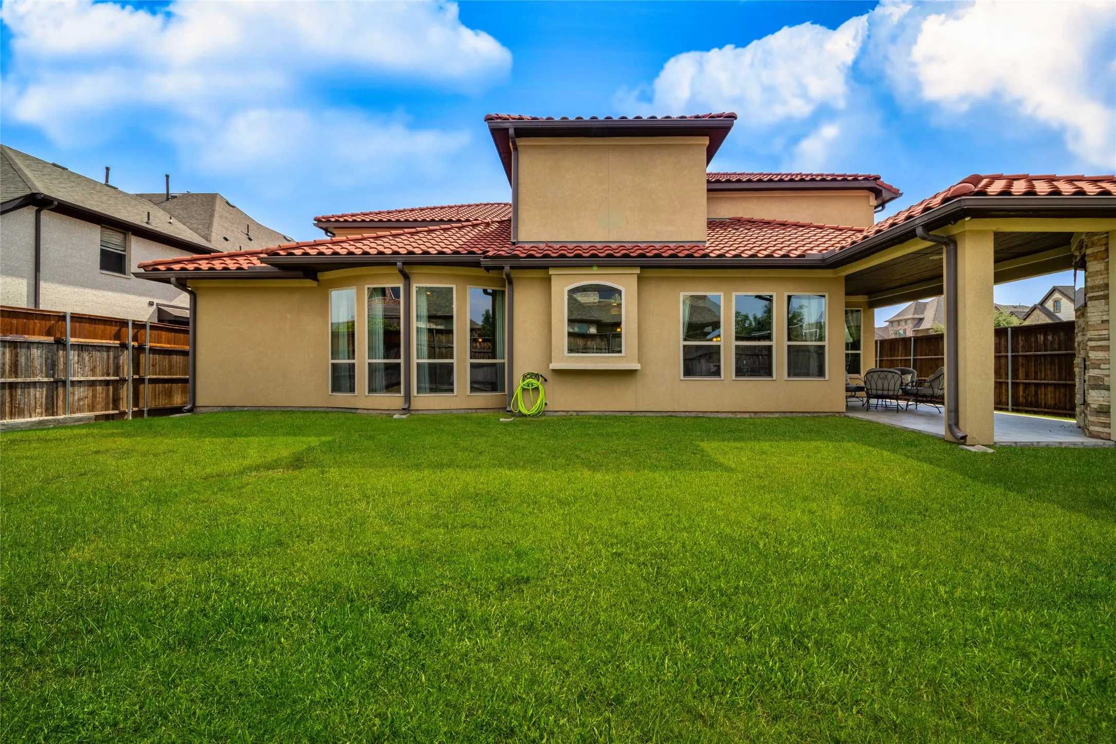 Spacious grassy yard with a covered patio, stucco exterior, multiple large windows, and a terracotta tile roof
