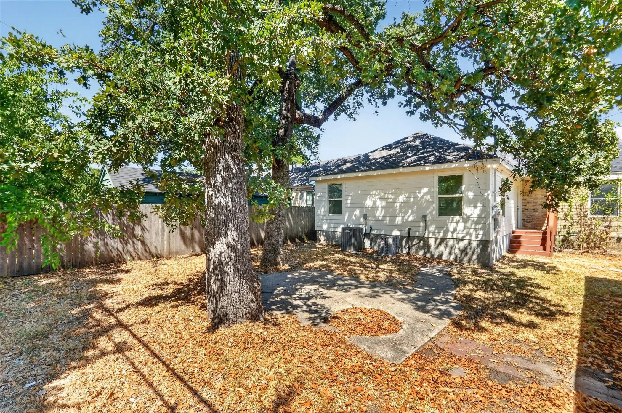 Expansive backyard featuring mature trees, a privacy fence, a concrete patio, and a shingled roof
