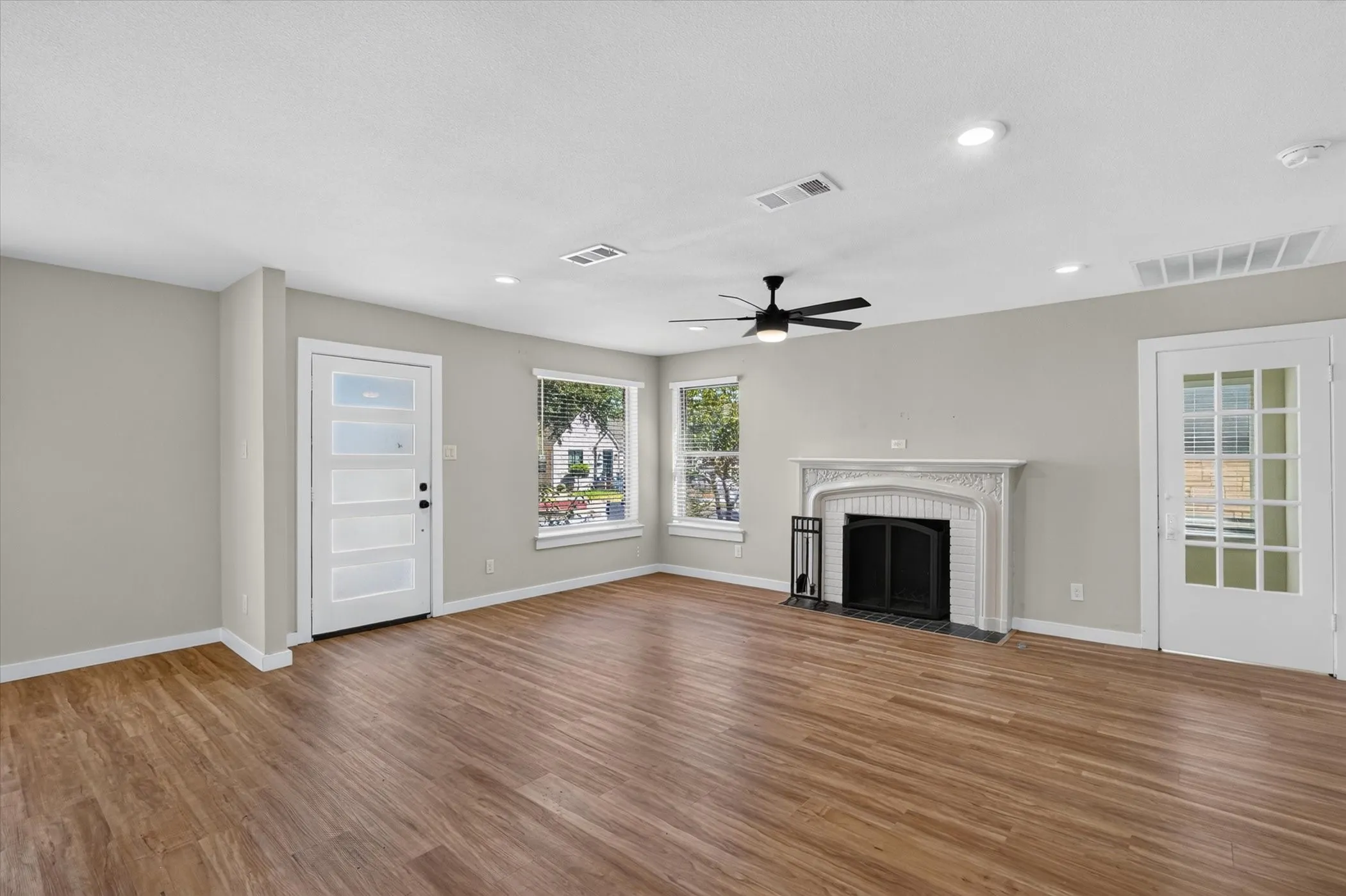 Wood-finish flooring, decorative fireplace, ceiling fan, recessed lighting, and a white modern panel door