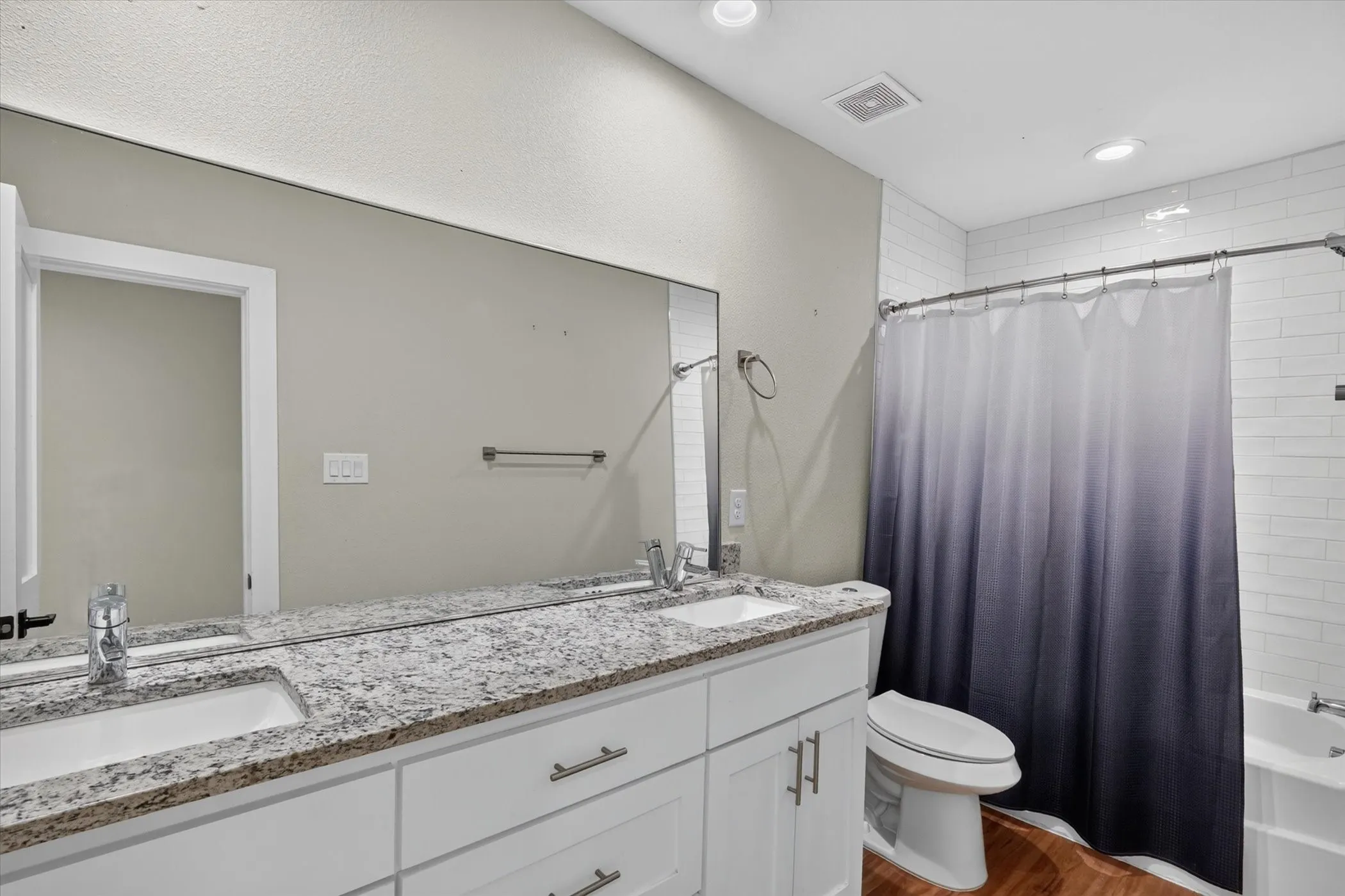 Dual vanity with integrated sinks, granite countertop, white cabinetry, and wood-finish flooring