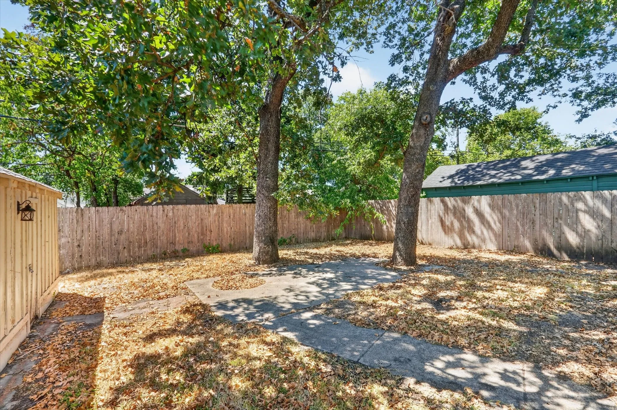Expansive backyard featuring mature trees, a privacy fence, and a concrete pathway
