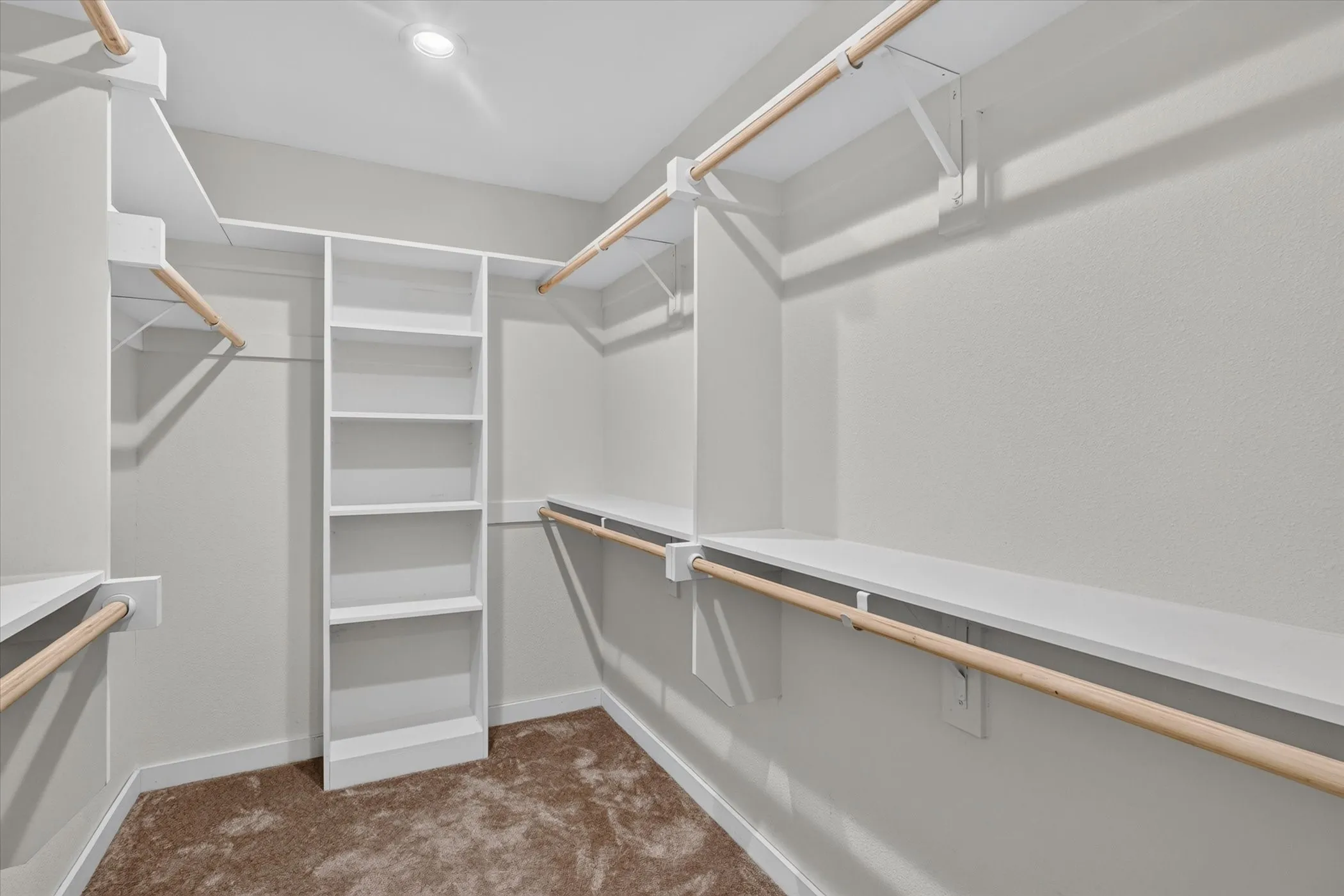 Recessed lighting illuminates a walk-in closet featuring built-in shelving, multiple hanging rods, and integrated upper storage