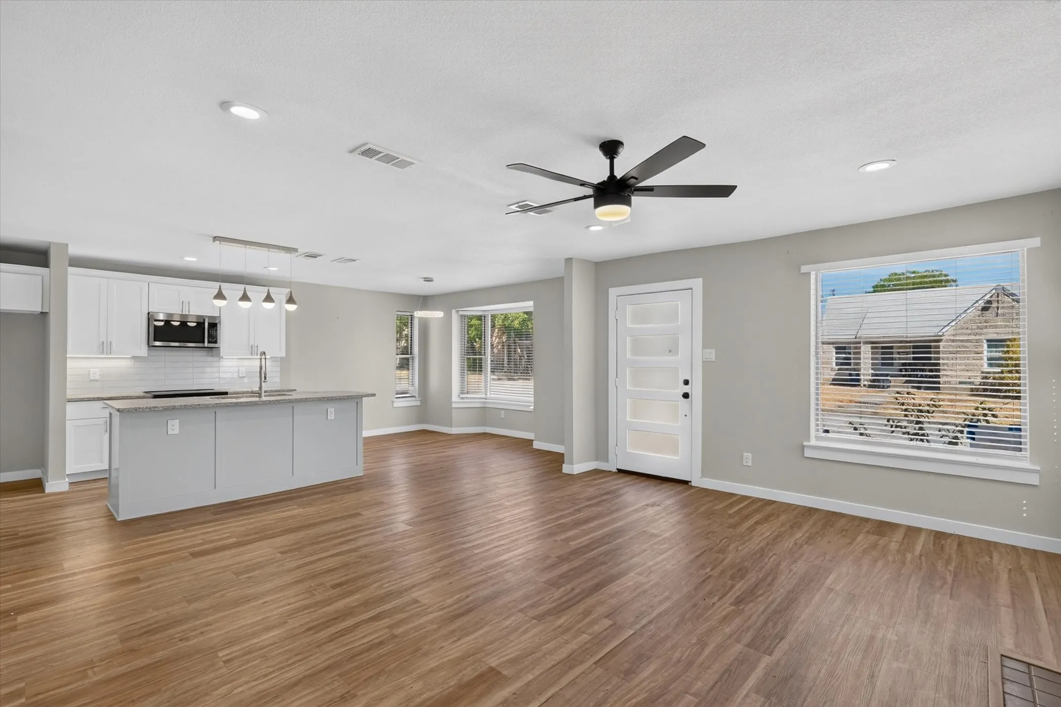 Wood-finish flooring throughout, modern kitchen island with an undermount sink, white shaker cabinetry, stainless steel appliances, and recessed lighting