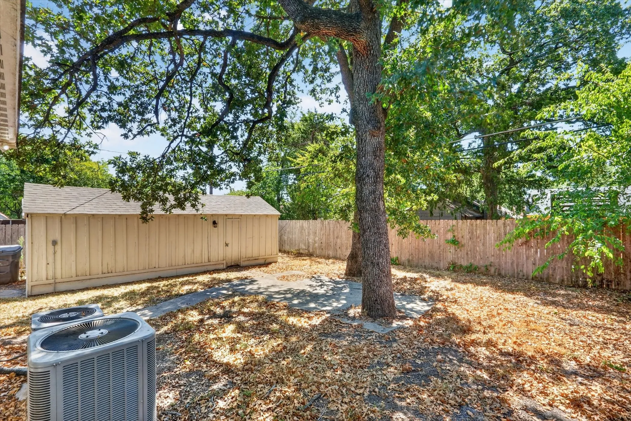 Expansive backyard featuring mature trees, a storage shed, and a privacy fence