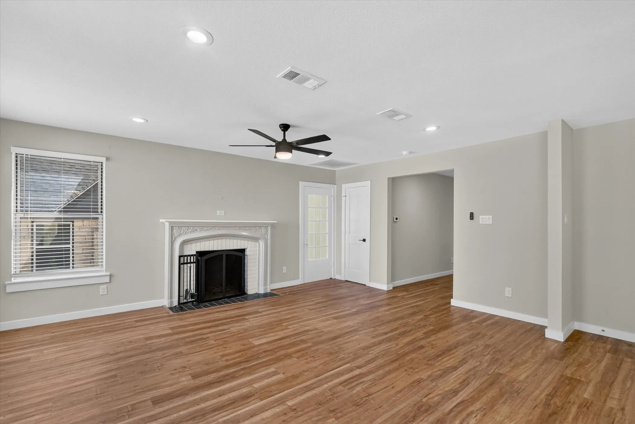 Wood-finish flooring throughout, featuring a decorative fireplace with a black iron grate, recessed ceiling lighting, and a ceiling fan