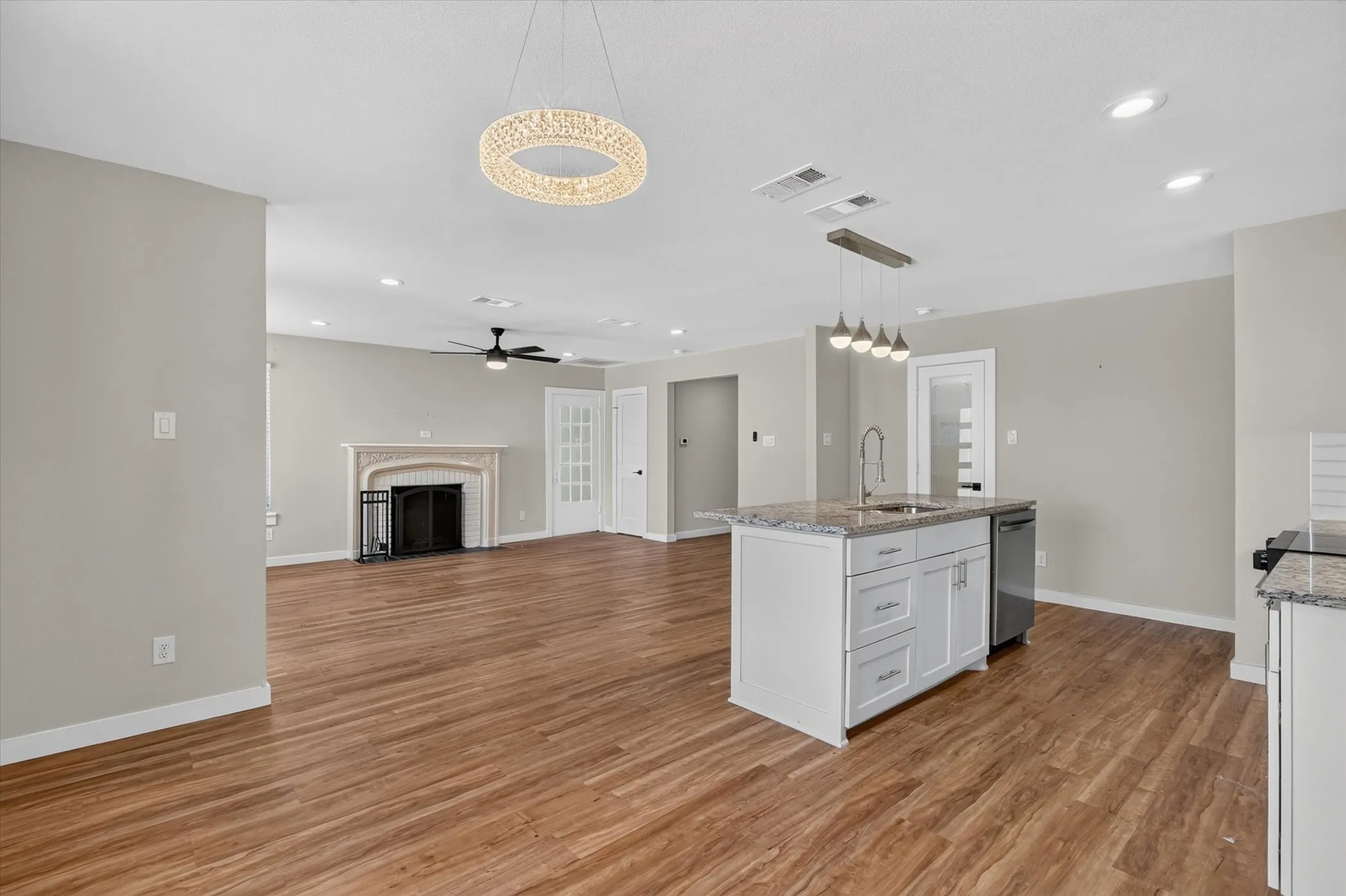 Wood-finish flooring, central island with granite countertop and stainless steel sink, built-in dishwasher, recessed lighting, and a decorative fireplace with mantel
