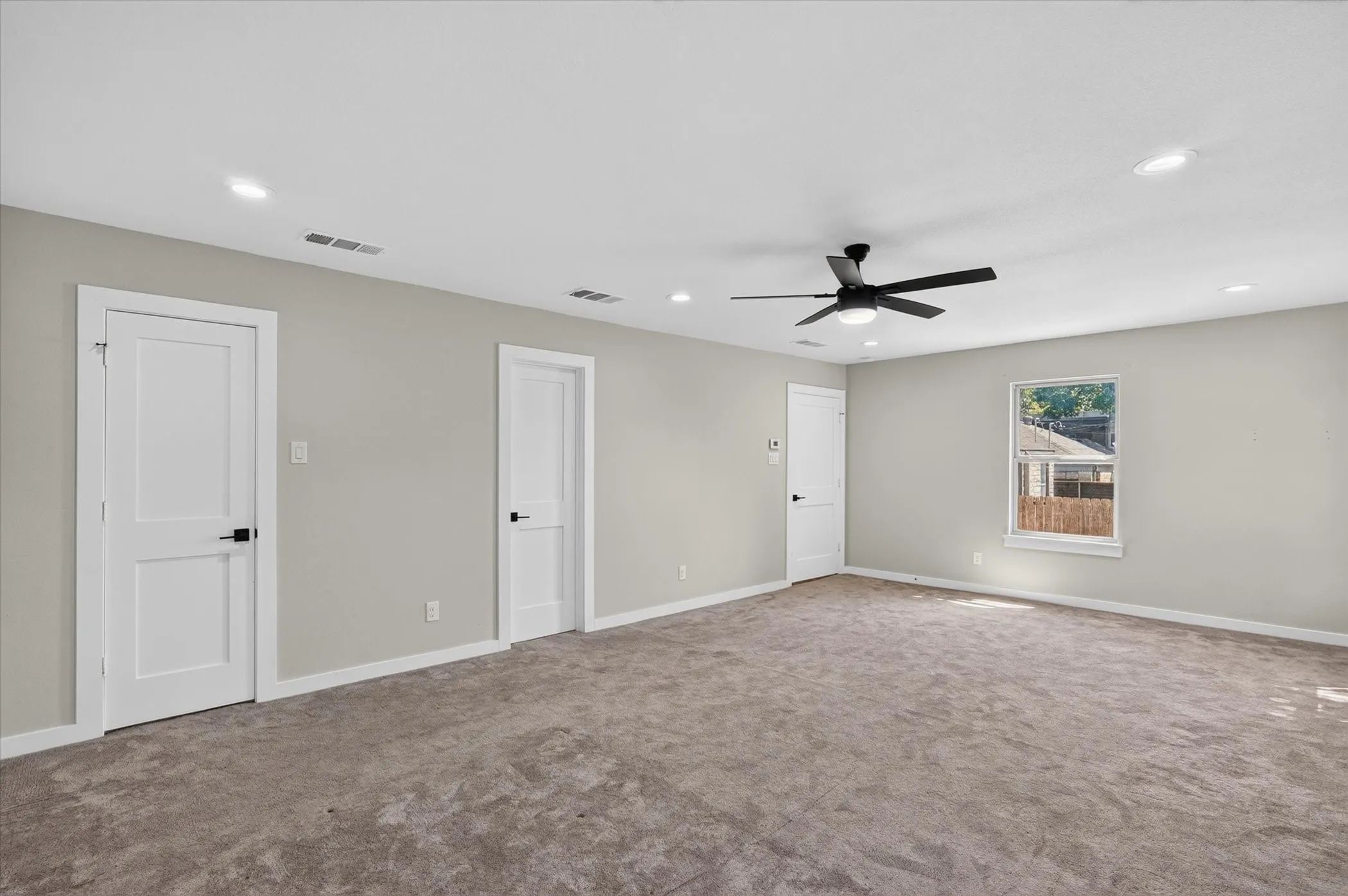 Spacious room with plush carpeting, recessed lighting, a ceiling fan, and multiple paneled doors