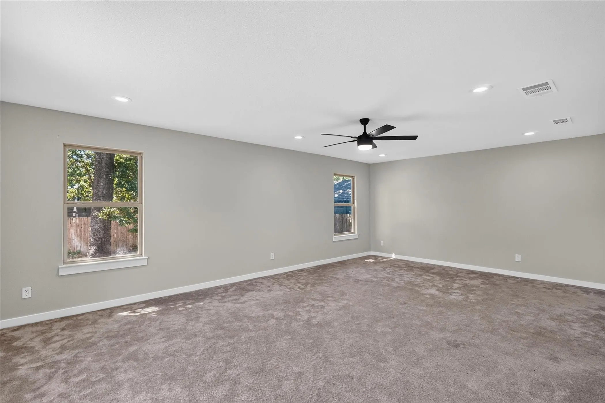 Spacious room featuring gray carpet, light gray wall paint, two windows, recessed lighting, and a ceiling fan