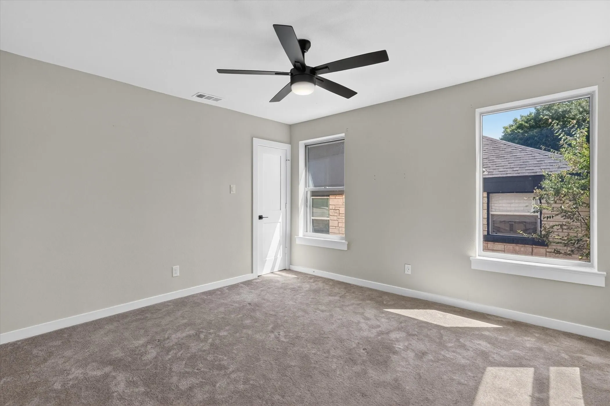 Neutral wall tones, gray carpeting, a modern ceiling fan with integrated lighting, a white panel door with black hardware, and multiple windows