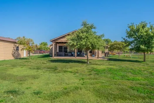 Expansive grassy yard with mature trees, a covered patio, and an outbuilding