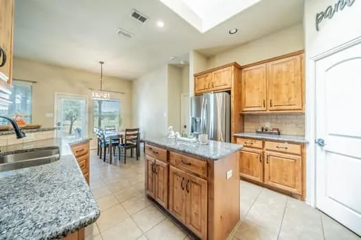 Kitchen featuring granite countertops, wood cabinetry, stainless steel refrigerator, tile flooring, and a skylight