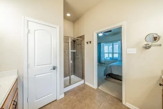 Tiled flooring, glass-enclosed shower, white paneled doors, and ceiling-mounted lighting