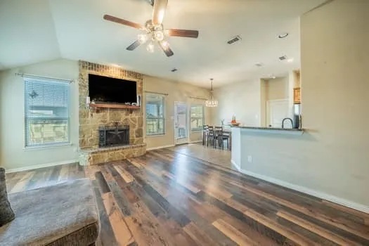 Vaulted ceiling, stone fireplace, wood-finish flooring, recessed lighting, and a breakfast bar