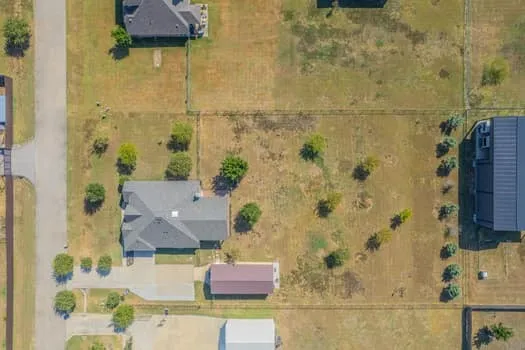 Expansive lot featuring a single-story residence with a dark shingle roof, paved driveway, detached outbuilding with a brown roof, and scattered mature trees