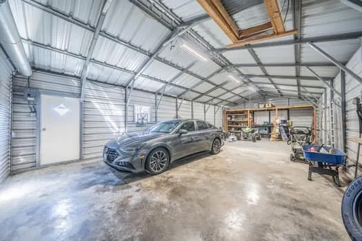 Spacious metal garage featuring a concrete floor, built-in shelving, and overhead lighting, includes a side door