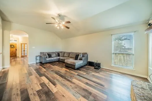 Vaulted ceiling, wood-finish flooring, ceiling fan, arched doorway, window with blinds