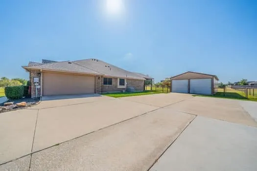 Brick exterior with an attached two-car garage, expansive concrete driveway, and a detached two-bay metal garage