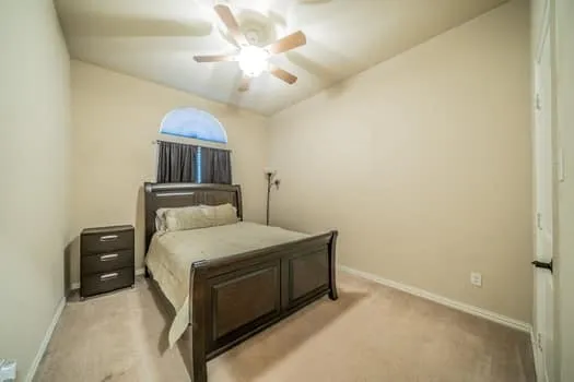 Arched window, vaulted ceiling, ceiling fan, and carpeted flooring