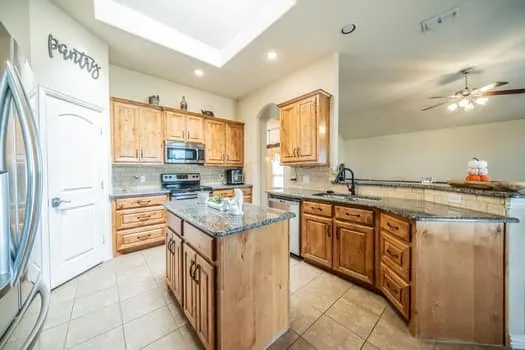 Kitchen with wood cabinetry, granite countertops, stainless steel appliances, and tile flooring