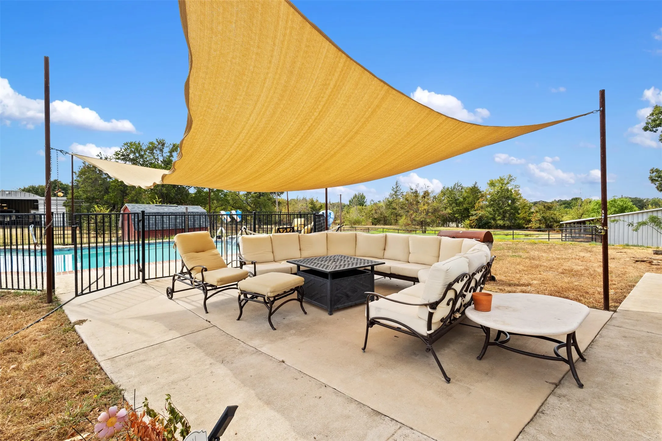 Expansive concrete patio with a shade sail, featuring a secure pool enclosure with black metal fencing