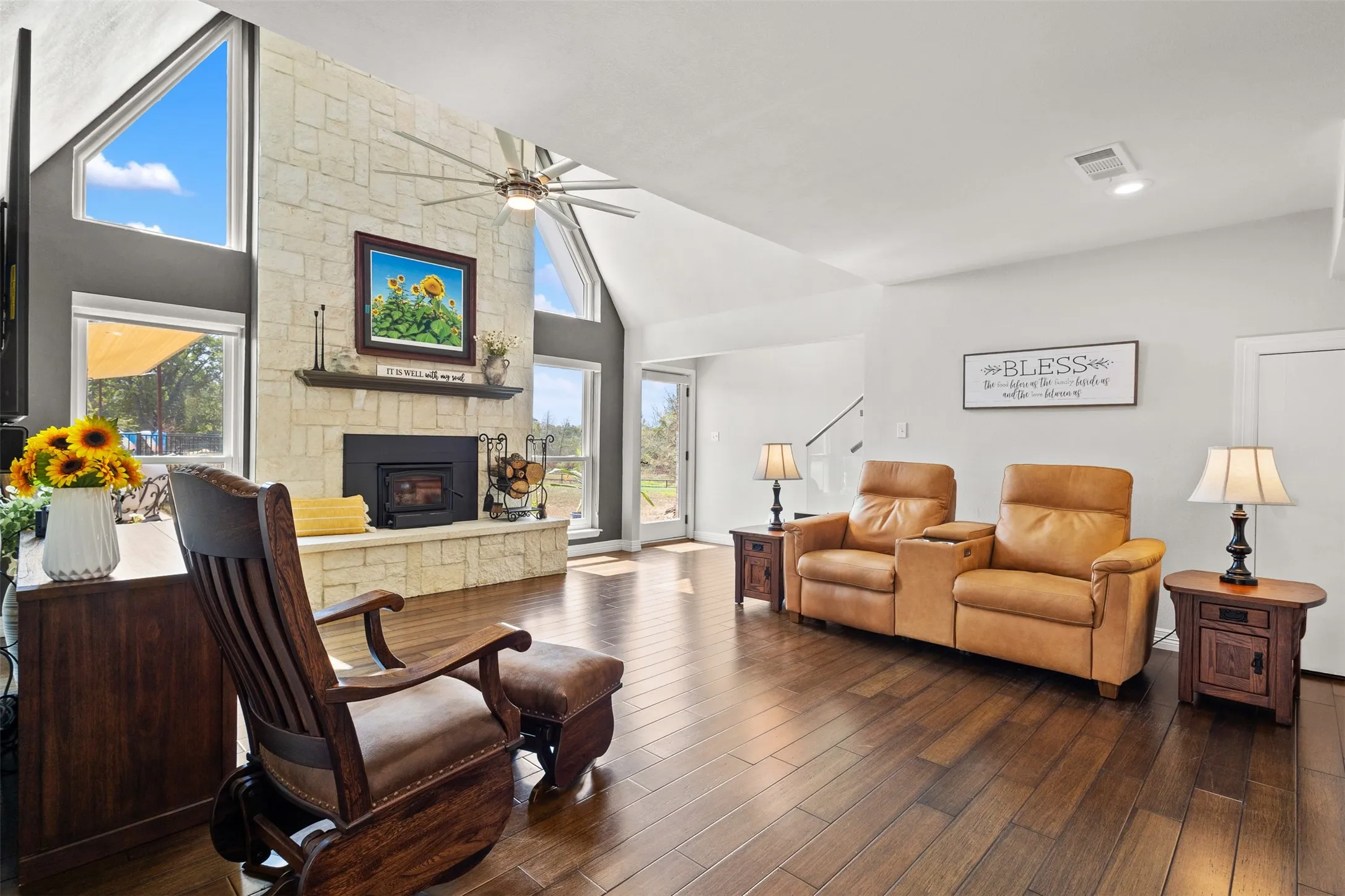 Vaulted ceiling with an exposed beam, stone-clad fireplace, wood-finish flooring, and large windows with architectural detailing