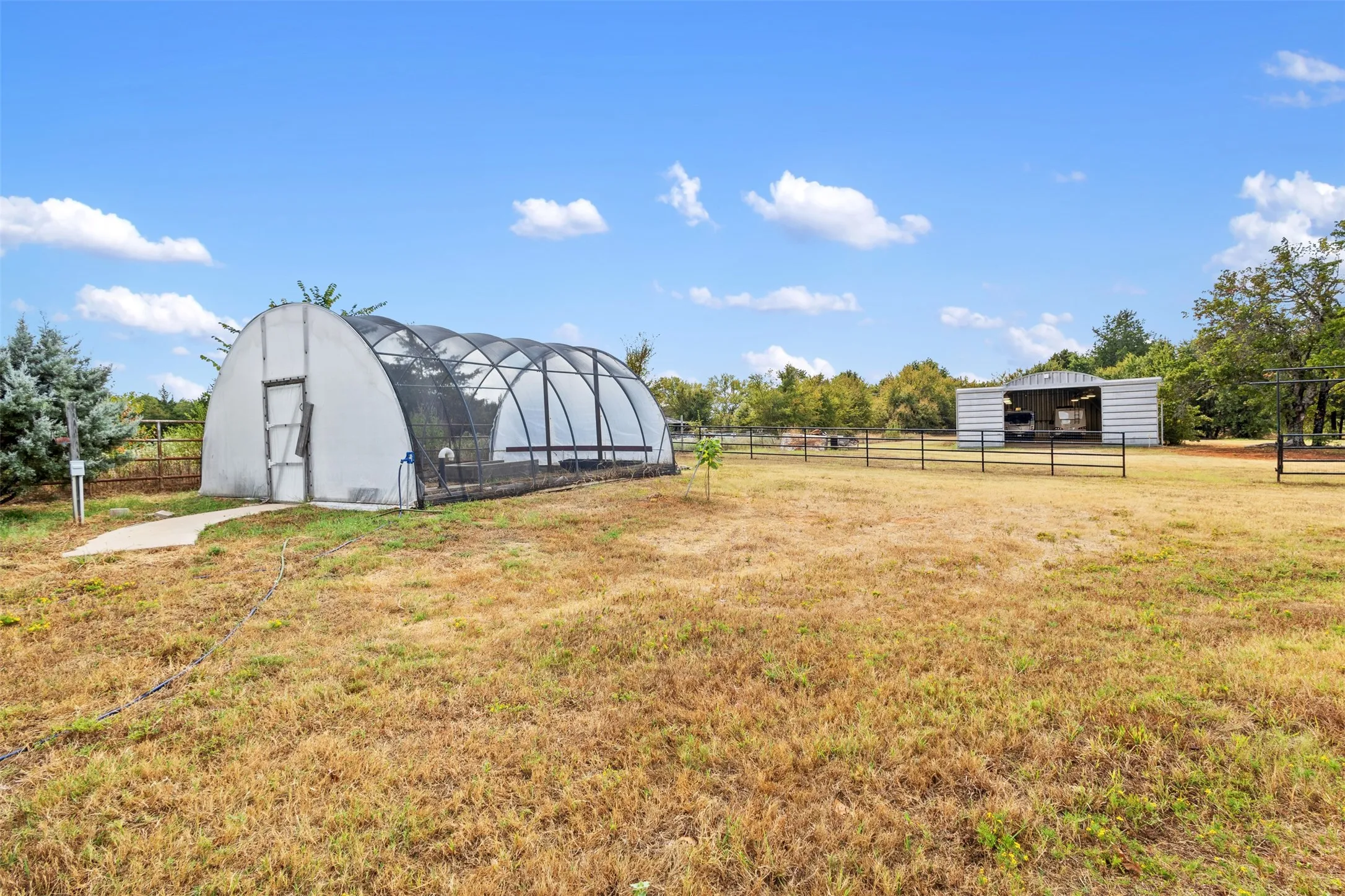Expansive grounds featuring a large greenhouse, metal utility building, and perimeter fencing