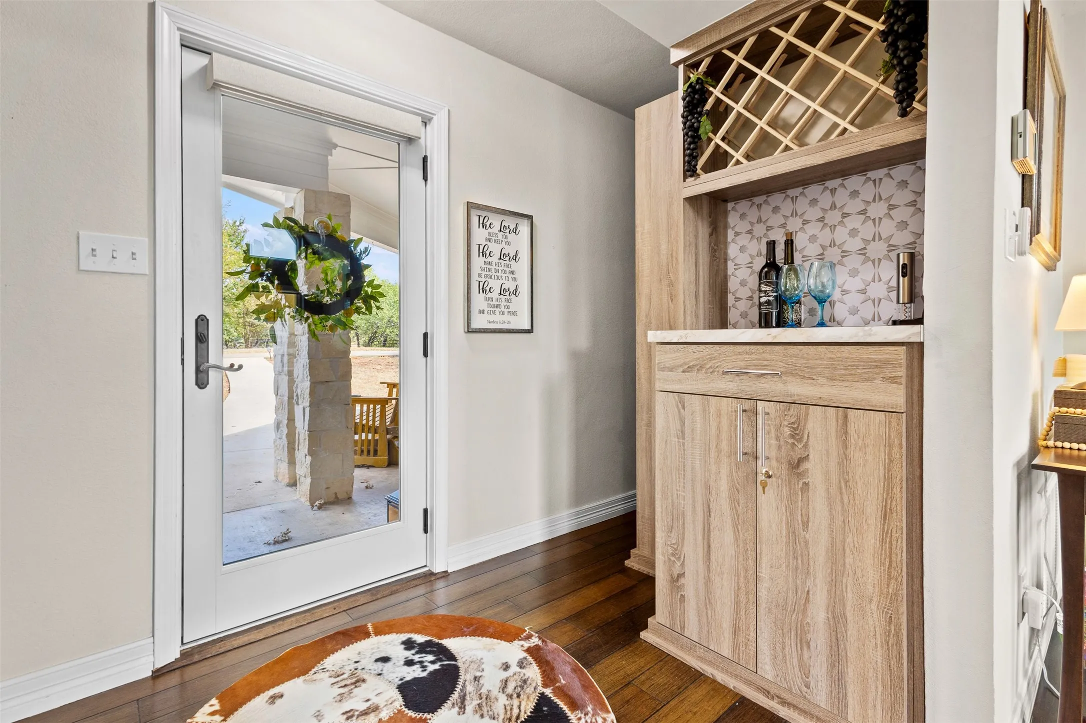 Hardwood-finish flooring, built-in dry bar with wine rack, light-toned cabinetry, light-toned countertop, and patterned tile backsplash