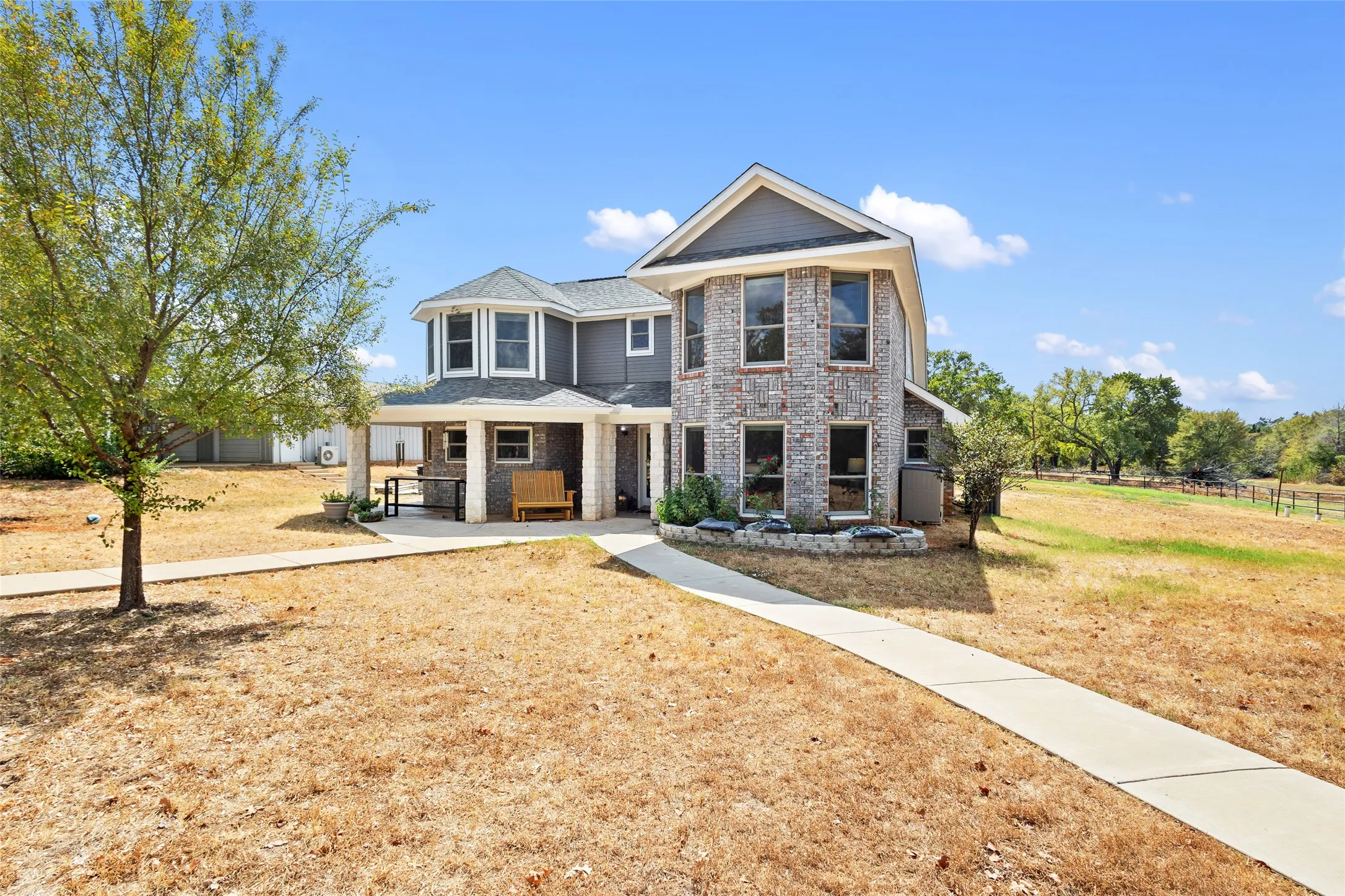 Two-story residence featuring a brick facade, gray siding, and a covered front porch with columns