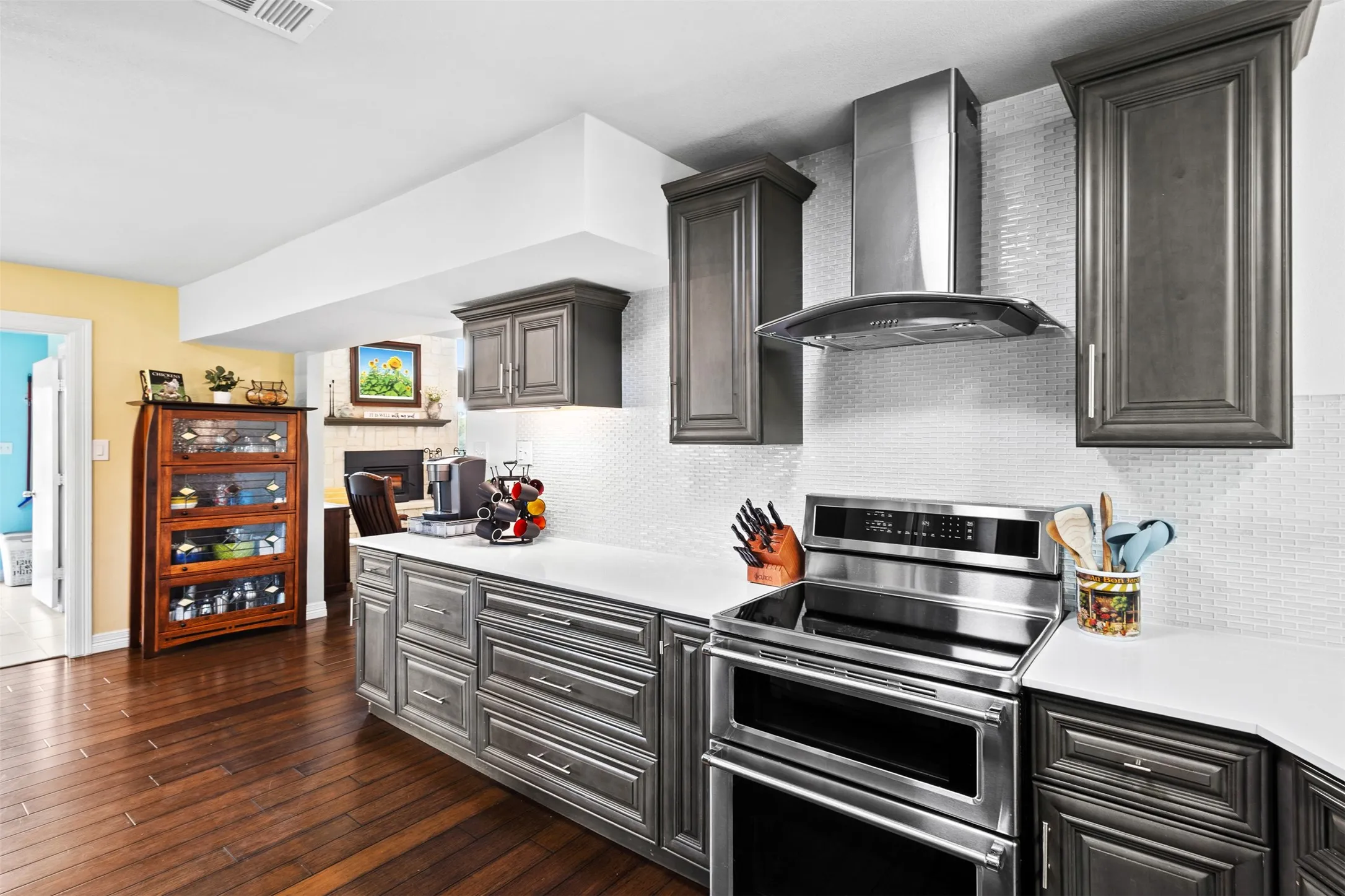 Dark wood-finish flooring, grey cabinetry with white countertops, stainless steel electric range with matching hood, and a white subway tile backsplash
