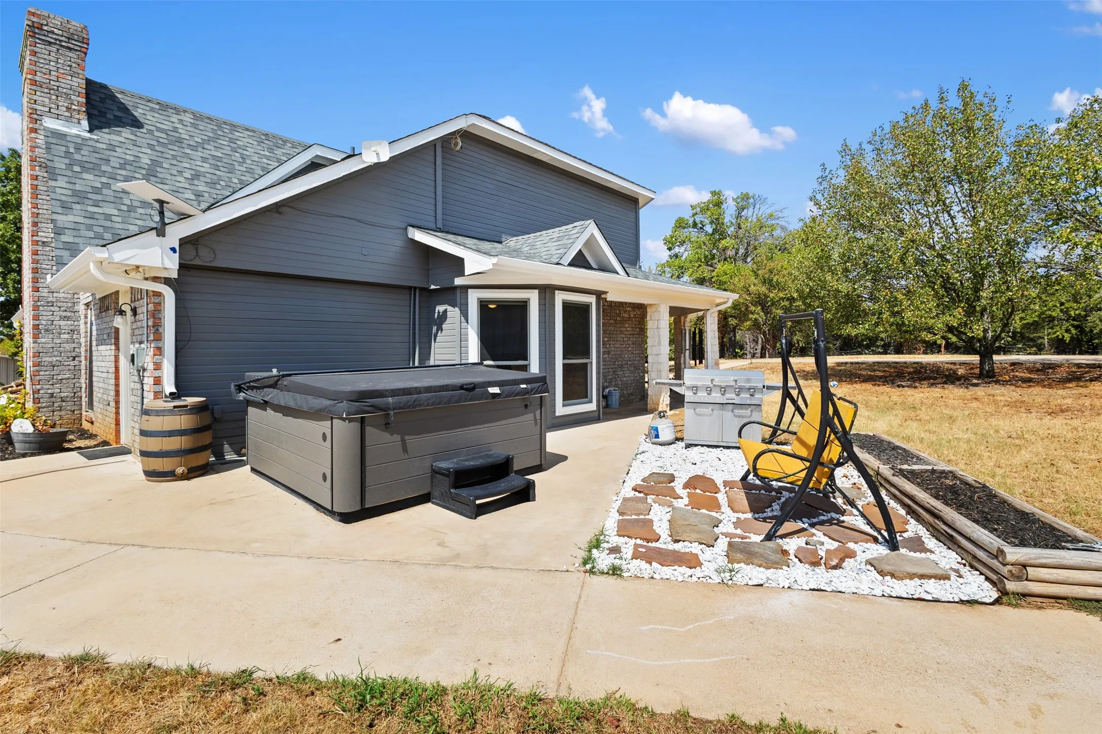 Exterior featuring a hot tub, concrete patio, stone accent pavers, and a raised planter bed