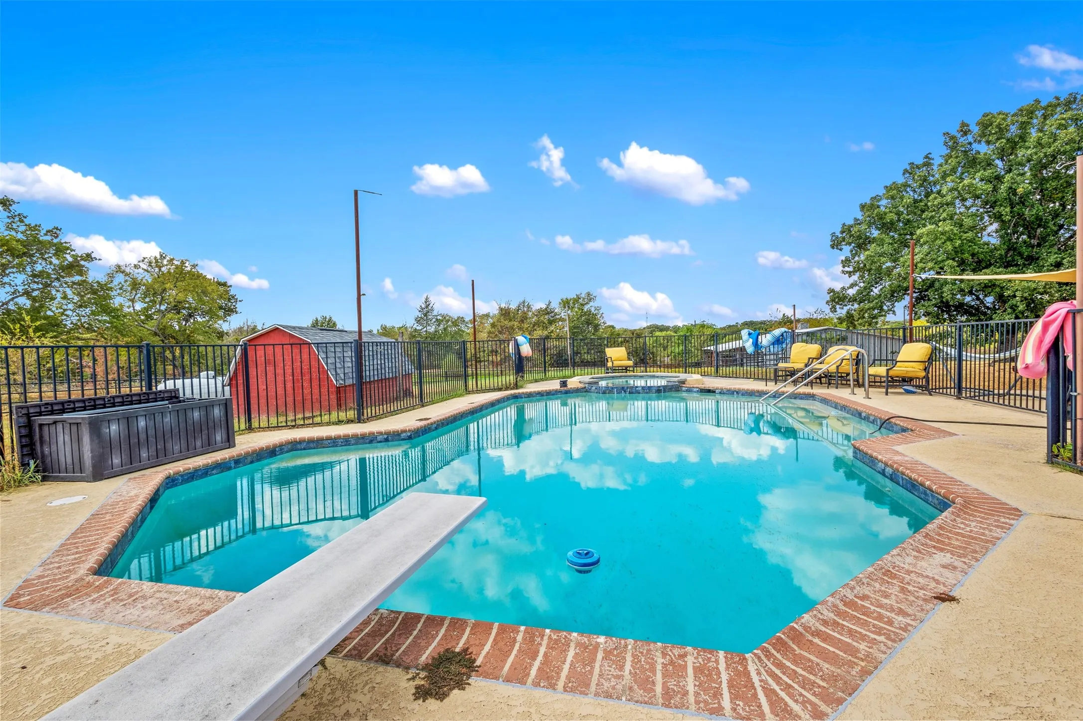 In-ground swimming pool with a diving board, surrounding concrete patio, and brick coping