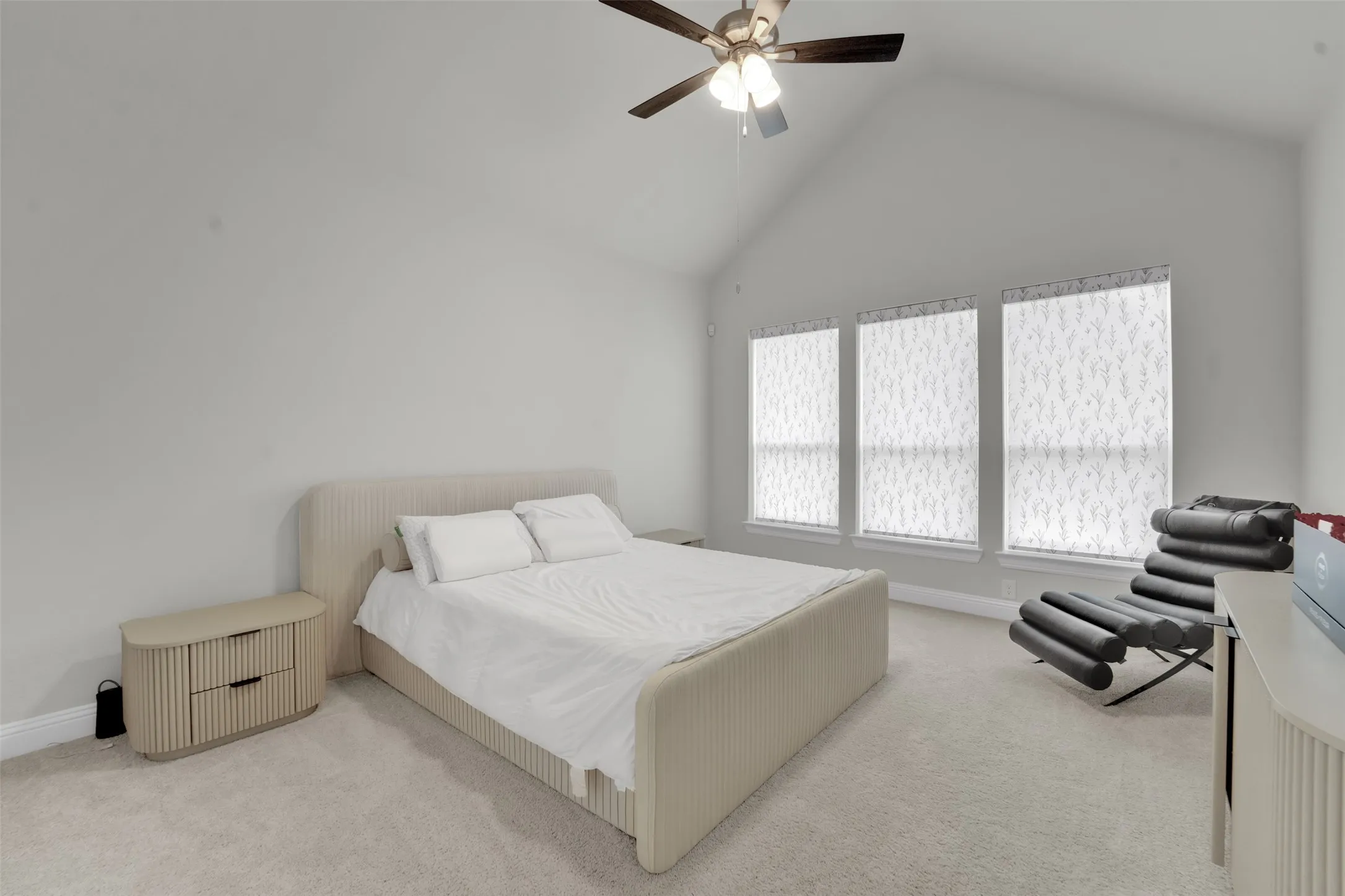 Vaulted ceiling featuring a ceiling fan with integrated lighting, three windows with roller shades, and light-toned carpeting