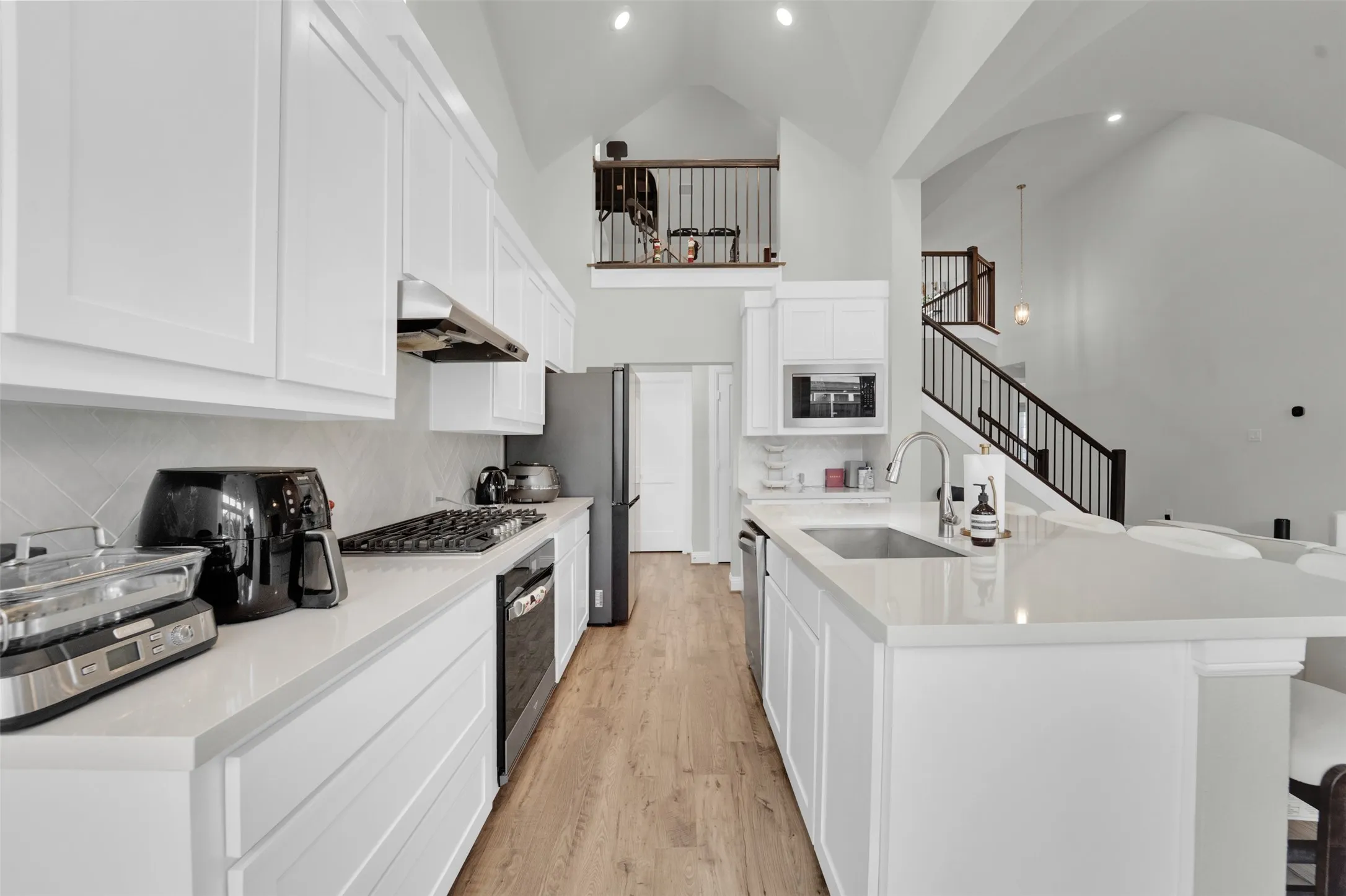 Kitchen featuring white cabinetry, light-toned countertops, a stainless steel sink, and wood-finish flooring