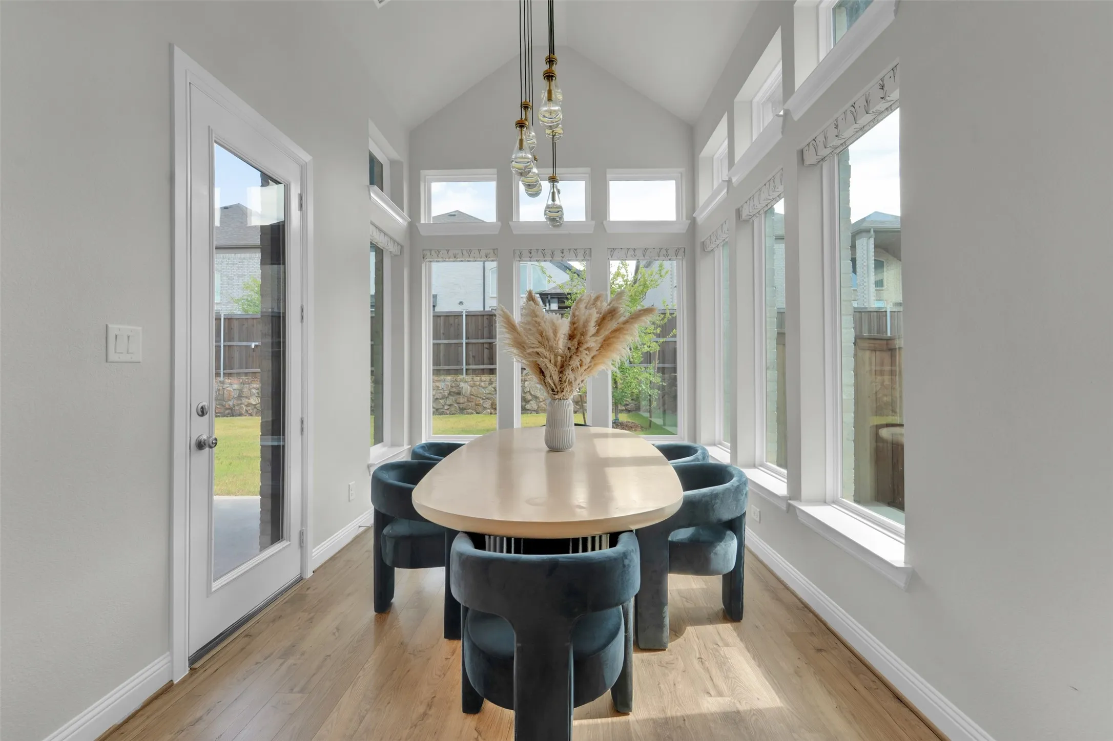 Vaulted ceiling, wood-finish flooring, full-light door, multiple tall windows, and a multi-bulb linear chandelier